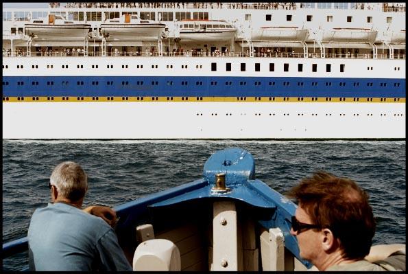 two men on a ferry on Sydney harbour with an ocean liner passing