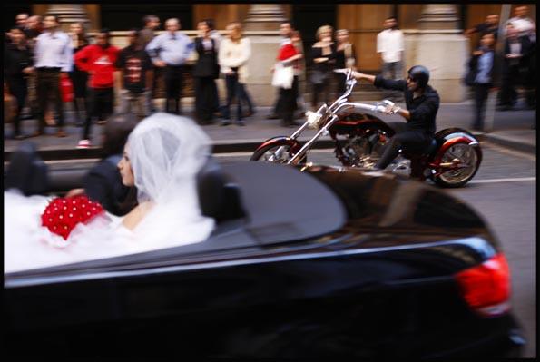 wedding party taking off just married couple in a convertible, accompanied by a motor bike rider