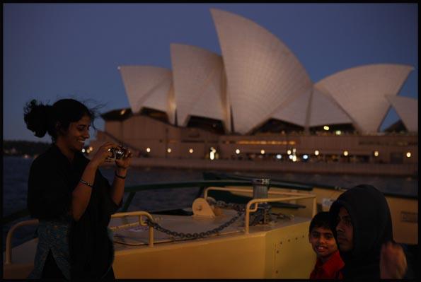 taking photos on a ferry before the backdrop of the Opera House